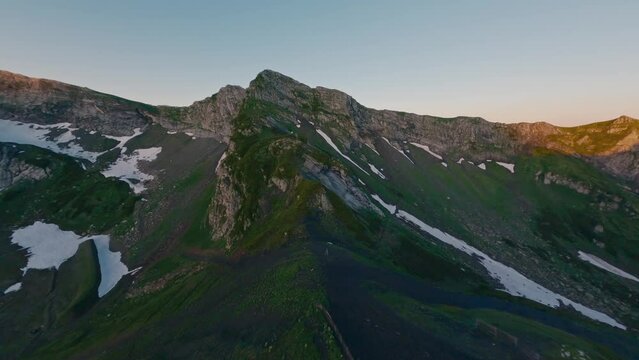 Aerial view mountain ridge peak ski resort cable car extreme close rock natural wall stone texture snow sunset. FPV sport drone amazing shot cliff alpine valley morning sunrise grass landscape pillar
