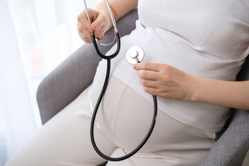 A pregnant woman uses a stethoscope.