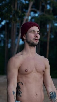 Young half naked sportsman warming up and training in pine forest during the winter. Deep breathing exercise.