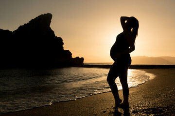 pregnant woman on the beach with backlit sunset and a hat