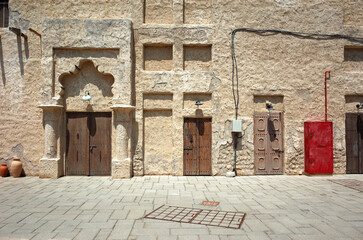 Old Dubai historical neighbourhood architectural detail, brown sandy color rough plastered wall with heritage wooden door fronts, United Arab Emirates