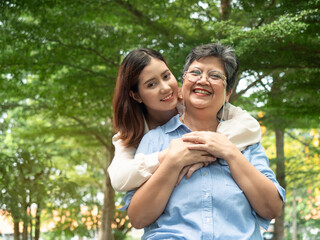 Naklejka premium Happy smiling young daughter hugging with senior mother at park and looking camera. Mother day concept. family concept