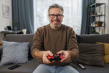 Portrait of happy man pushing buttons on joystick to play video game on sofa in the room