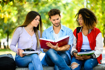 Fototapeta na wymiar Three multiethnic students studying together sitting on a bench outdoor