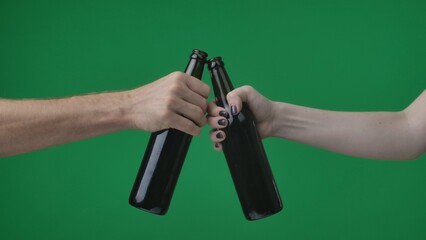 In a close up shot against a green background. a womans and a mans hand holding bottles of beer,...