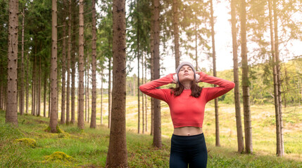 Sporty woman runner training outdoors in a forest, listening to music with headphones