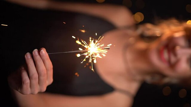 Celebration party with black background. girl holding sparkler and smiling. new year or birthday party celebration evening. Vertical reel format slow motion video footage