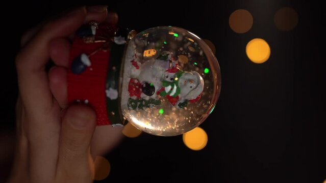 Glass ball toy. Winter traditional snow symbol.  Woman hand holding Christmas symbol Cristal snow globe. Slow motion vertical reel video footage. hand held camera