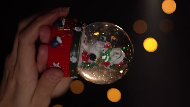 Winter traditional snow symbol. Glass ball toy. Woman hand holding Christmas symbol Cristal snow globe. Slow motion vertical reel video footage. hand held camera
