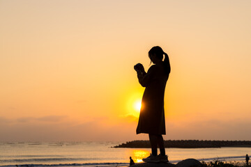 Silhouette of woman stand at sunset in the beach and use digital camera to take photo