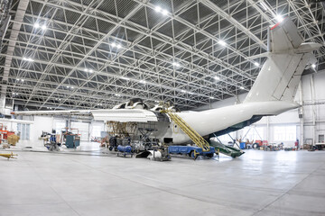 White transport aircraft in the aviation hangar. Airplane under maintenance. Checking mechanical...