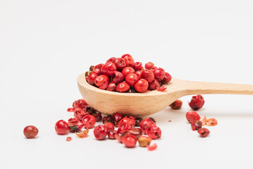 Pink peppercorns in a wooden spoon on a white background isolated