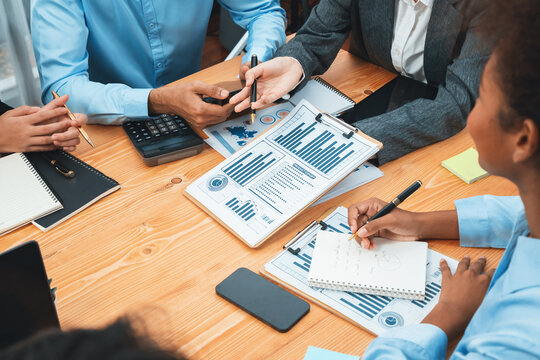 Multiracial analyst team use BI dashboard data to analyze financial report on meeting table. Group of diverse business people utilize data analysis by FIntech for business marketing decision. Concord