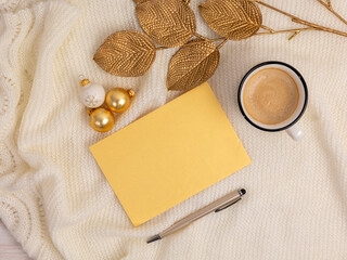 Card flat lay mockup with golden leaves and Christmas balls, coffee pen on soft cozy fabric background. Christmas or Winter style. Top view.