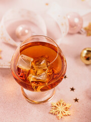 Glass of whiskey or bourbon with festive Christmas decoration on light beige background. New Year, Christmas and winter holidays whiskey mood concept