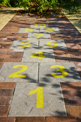 Hopscotch kids game on brick path with yellow numbers and shadow of leaves on sidewalk