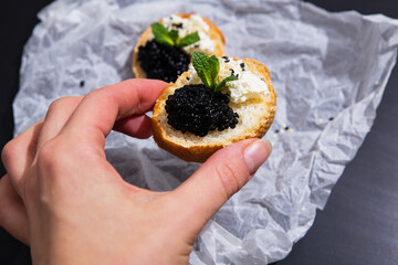 Black caviar - fine dining, wealthy eating concept. Crispy canape with black caviar in woman's...