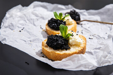 Crispy canapes with black caviar, soft cream cheese and sprigs of mint, silver spoon of caviar. A...