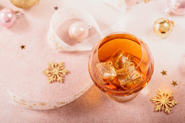 Glass of whiskey or bourbon with festive Christmas decoration on light beige background. New Year, Christmas and winter holidays whiskey mood concept
