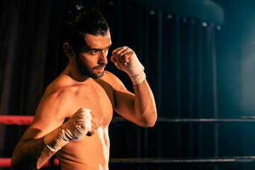 Boxing fighter shirtless posing, caucasian boxer punch his bare fist and wrap in front of camera, aggressive stance and ready to fight at the boxing ring. Impetus