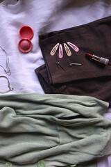 Pastel green cardigan, white shirt, gray trousers, black loafers, various silver jewelry, perfume and make-up products. Outfit concept, top view.