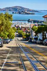 Empty street with rails for streetcars leading to Alcatraz Island on sunny day with pier, San Francisco, CA