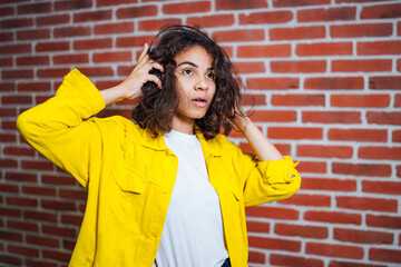 A woman in a yellow jacket is standing near a brick wall. The Vibrant Woman in a Yellow Jacket Poses Gracefully Against a Textured Brick Wall