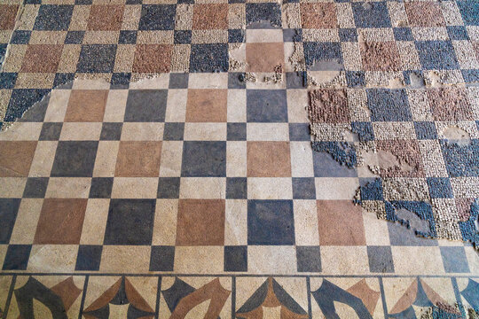Archaeological remains of floor painted with colored square figures and above restored remains of Roman mosaic with geometric figures, red and blue squares forming a checkerboard on the floor.