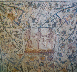 Archaeological remains of a Roman mosaic of three men in loincloths holding hands crushing grapes to make wine, with vines and animals as decoration. Mérida archaeological complex.