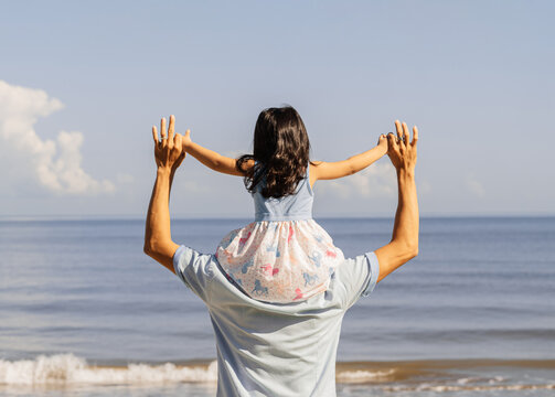 Fun father holding a his daugther over head walking to a beach.