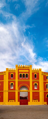Red and yellow facade of the Bullring in Mérida, Extremadura in Spain, under a blue sky with white...