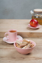 Coffee in a pink cup and saucer is on the table. There are cookies and jam nearby.