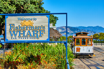 Welcome sign for Fisherman’s Wharf, San Francisco and trolley with tourists and mountain