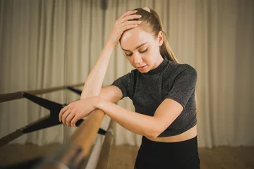 Foto auf Acrylglas Tanzschule Upset ballerina in training suit stands near ballet barre and looks at the mirror in dance studio. Woman prepares for performance. Ballet dancer doing gymnastic exercises. Classical ballet school