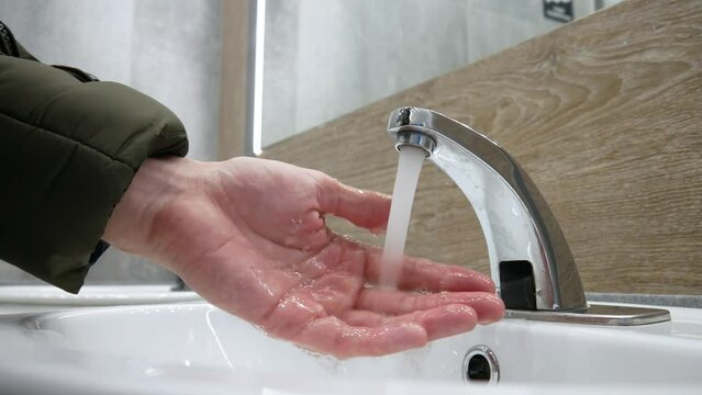 Close-up of a faucet in a restroom and a man washing the hands