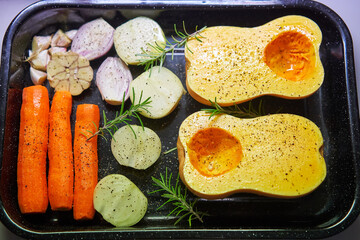 Food ingredients to cook delicious creamy pumpkin soup in the roasting pan sprinkled by black pepper and salt consist trom shallot, onion, carrot, head of garlic and pumpkin with fresh green rosemary.