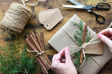 Wrapping present in brown paper twine with evergreen and cinnamon stick accent, natural winter...