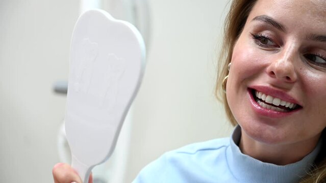 Young Beautiful woman smile after Dental Whitening process smile in mirror. Teeth whitening with UF Lamp, Led Lamp and gel in Dental Clinic. 4k 120 fps slow motion Raw footage
