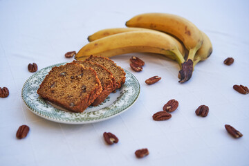Three slices of freshly baked delicious banana bread on the small vintage porcelain plate with bunch of bananas from organic farming and pekan nuts. Ideal dish for low carb diet or healthy lifestyle.
