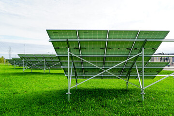 Naklejka premium Installation of solar panels on metal frames in a green meadow, unfinished solar power plant
