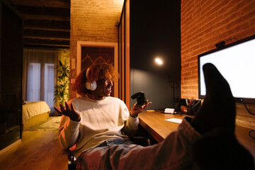 Young man with white headphones playing video games on a desk in a living room. Upset young man losing a game.