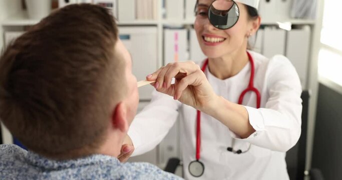 Doctor ent with frontal mirror examining patient throat with wooden spatula 4k movie slow motion. Diagnosis and treatment of chronic tonsillitis in adults concept