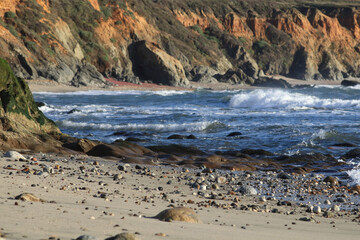 The waves are rolling on the shore. Small pebbles and sandy beach
