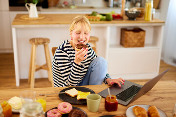 Young woman using laptop while enjoying breakfast  at home