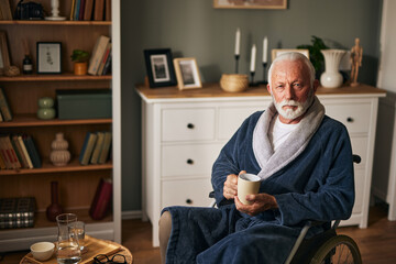 Elderly man sitting in wheelchair drinking coffee in the living room