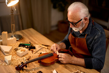 Senior carpenter craftsman carving wood and making violin instrument