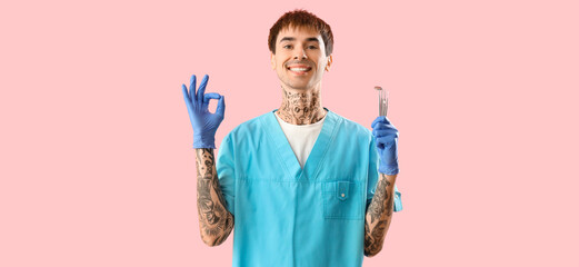 Male tattooed dentist with tools showing OK on pink background