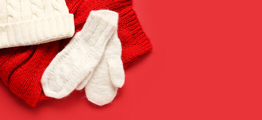 Pair of white knitted mittens with warm hat and scarf on red background with space for text