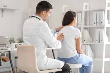 Male doctor checking posture of young woman in clinic - obrazy, fototapety, plakaty