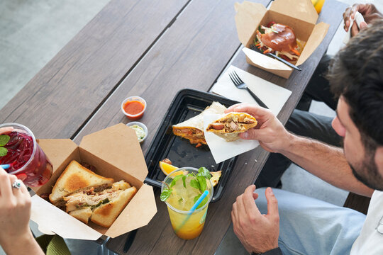 Friends eating takeout food at table burrito with bites takes